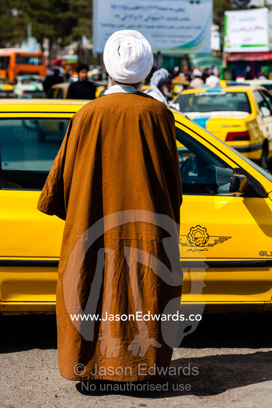 A member of the clergy wearing a turban and a woven cloak getting into a taxi. Fatima Masumeh Shrine, Qom, Qom Province, Islamic Republic of Iran.