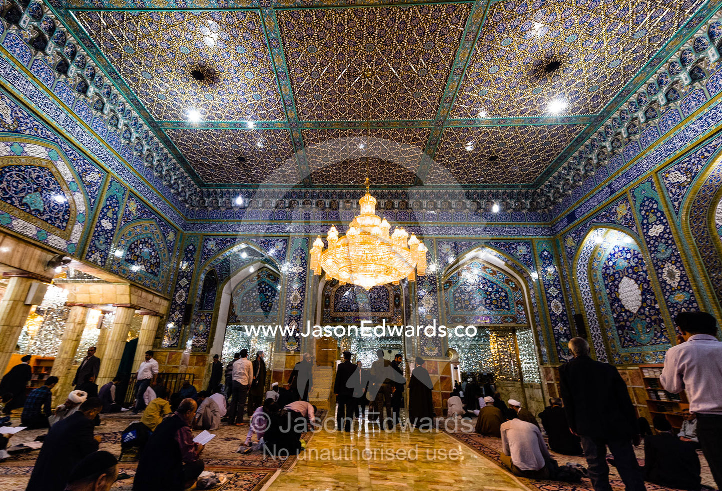 Men at prayer beneath the magnificent mirrored ceiling and chandelier of the Holy shrine of Hazrat Masuma. Fatima Masumeh Shrine, Qom, Qom Province, Islamic Republic of Iran.