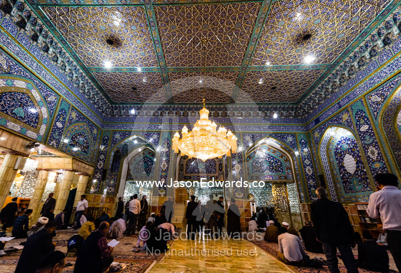 Men at prayer beneath the magnificent mirrored ceiling and chandelier of the Holy shrine of Hazrat Masuma. Fatima Masumeh Shrine, Qom, Qom Province, Islamic Republic of Iran.