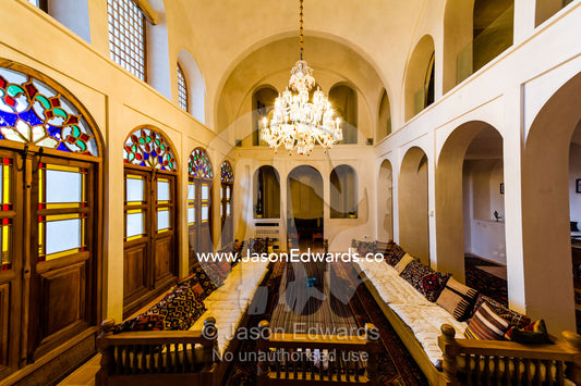 Long cushioned seats beneath a chandelier in a sitting room. Manuchehri house, Kashan, Isfahan, Islamic Republic of Iran.