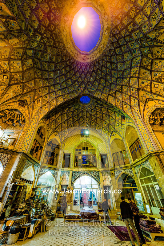 Carpet sellers and merchants display their wares beneath the vaulted spiralling geometric ceiling of an ancient bazaar. The Bazaar of Kashan, Kashan, Isfahan, Islamic Republic of Iran.