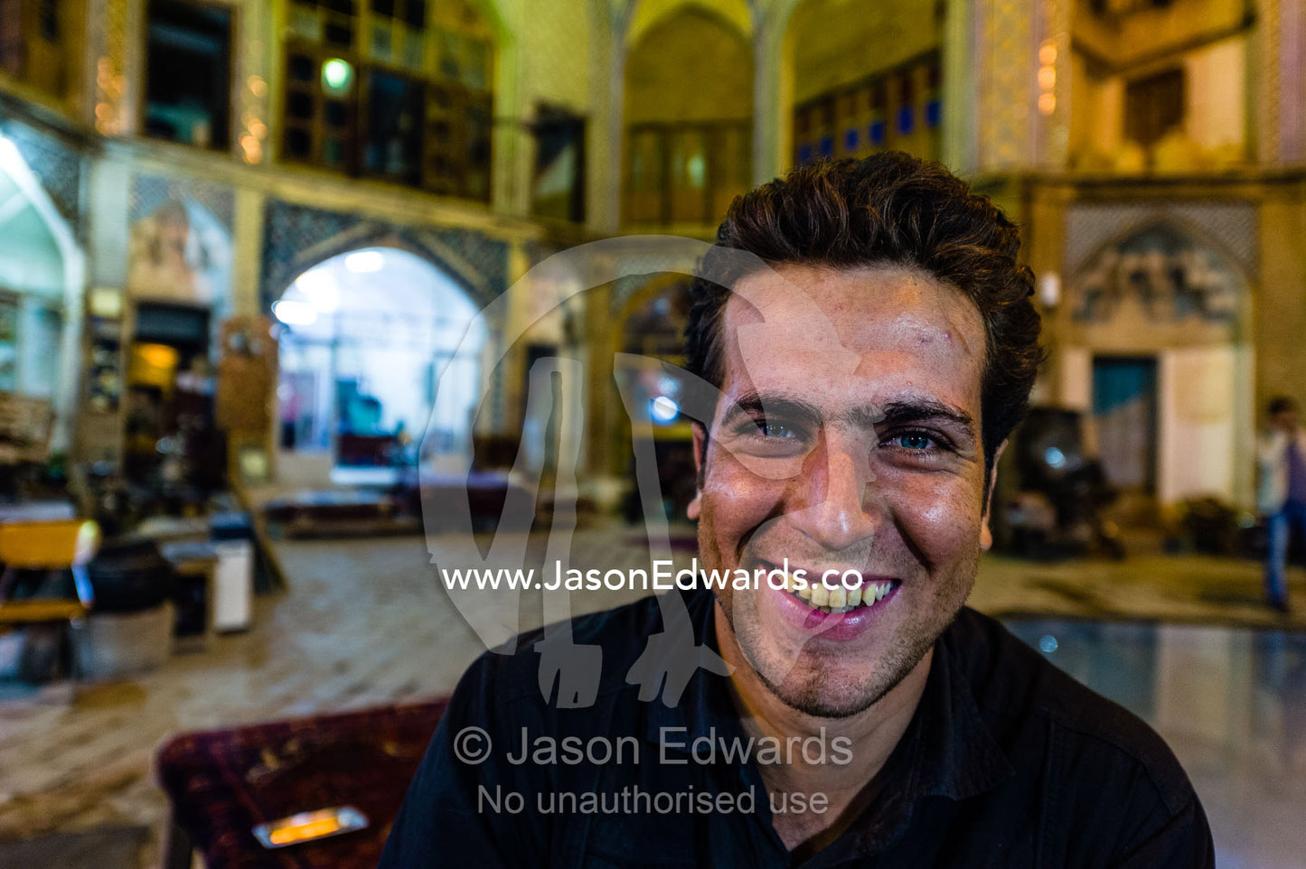 A smiling young man with a funky groomed hairstyle in an ancient bazaar. The Bazaar of Kashan, Kashan, Isfahan, Islamic Republic of Iran.