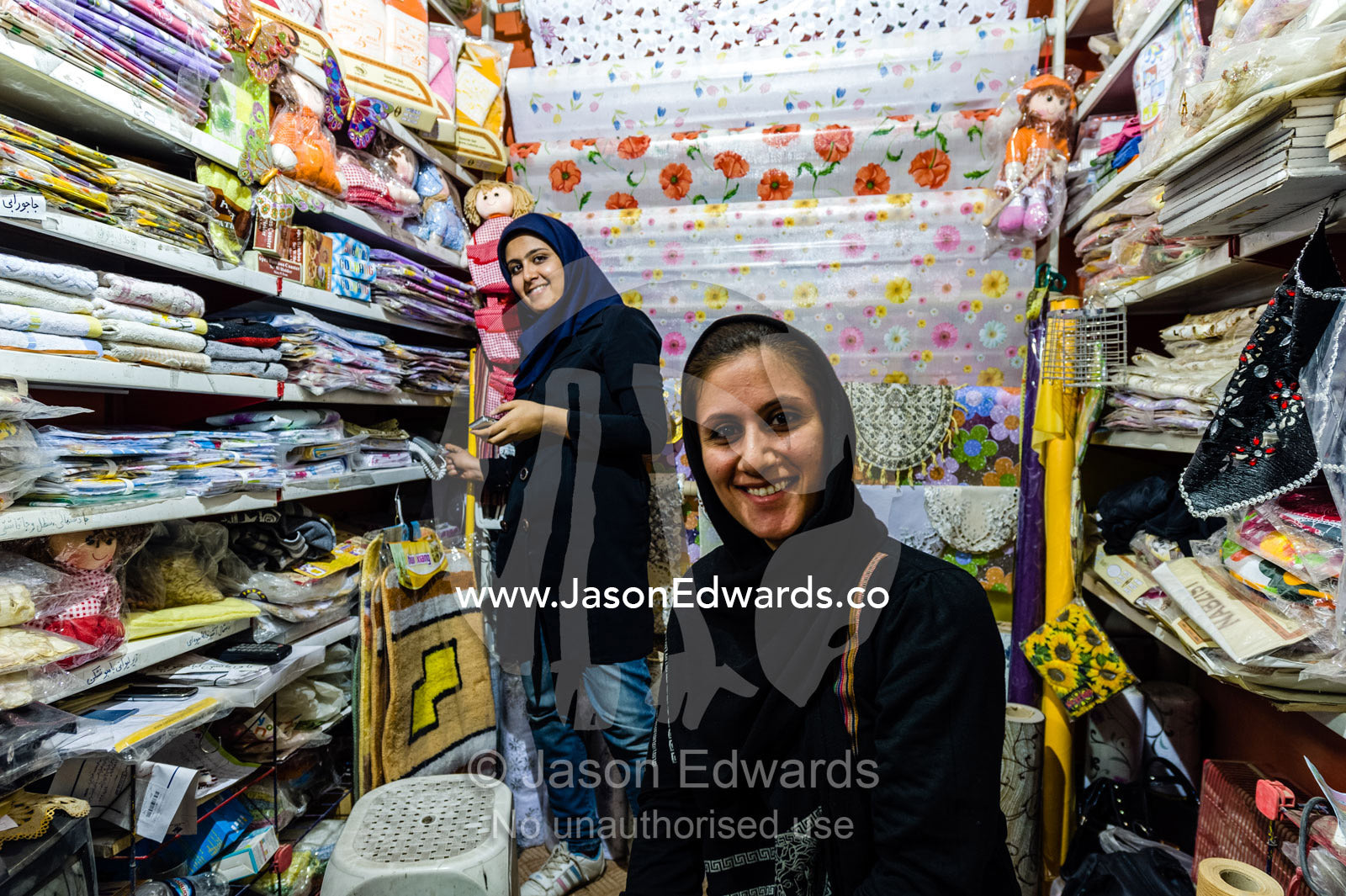 Shopkeepers selling household goods such as table cloths, floor matts and fabric in a bazaar. The Bazaar of Kashan, Kashan, Isfahan, Islamic Republic of Iran.