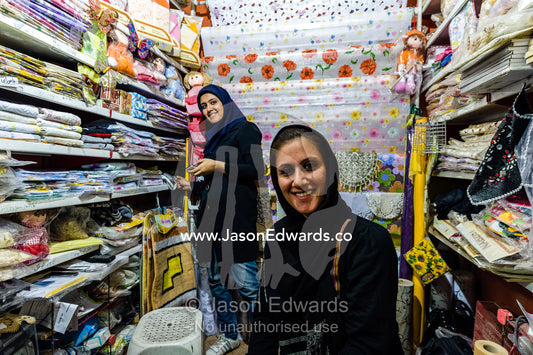 Shopkeepers selling household goods such as table cloths, floor matts and fabric in a bazaar. The Bazaar of Kashan, Kashan, Isfahan, Islamic Republic of Iran.