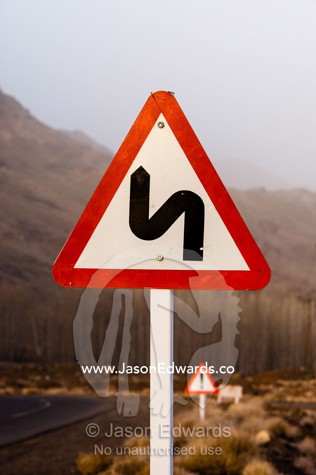 A sign warns of winding roads through a mountain pass. Abyaneh, Barzrud Rural District, Natanz County, Isfahan Province, Islamic Republic of Iran.