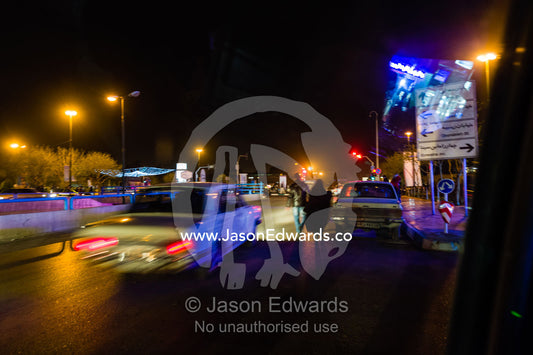 Speeding cars pass people walking along a road at night. Isfahan, Isfahan Province, Islamic Republic of Iran.