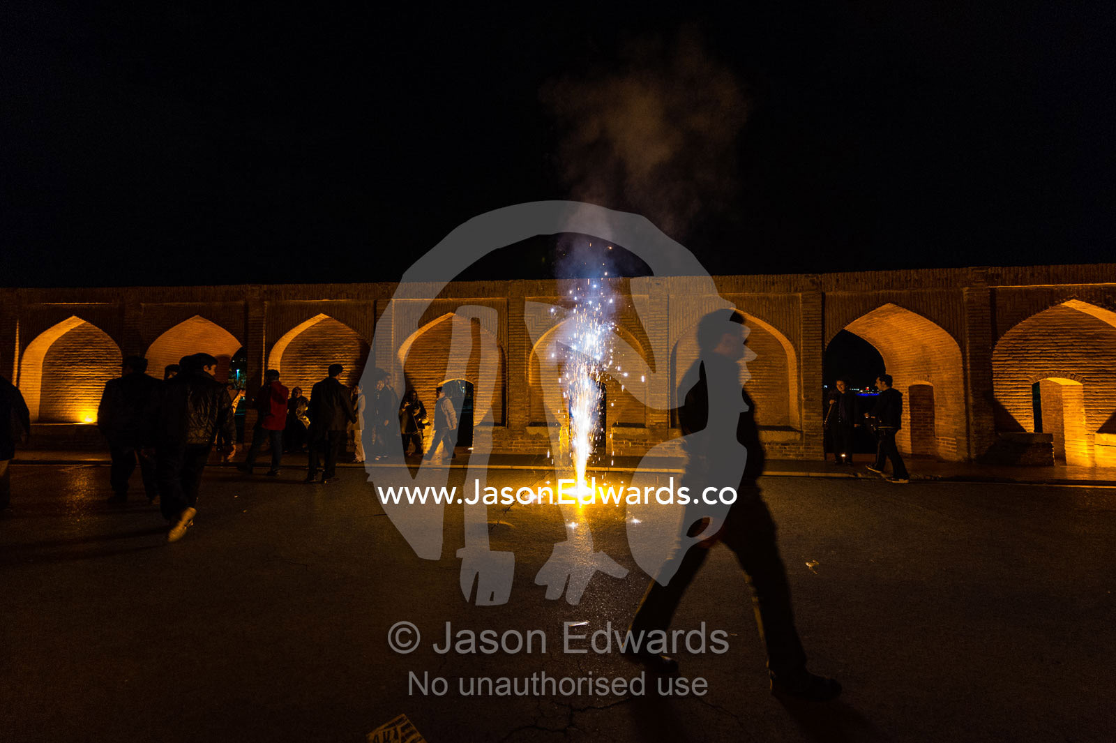 Light cascades from iwans lining the Khaju Bridge onto families and friends celebrating with fireworks during Nowruz Iranian New Year. Si-o-seh pol Bridge, Zayandeh River, Isfahan, Isfahan Province, Islamic Republic of Iran.