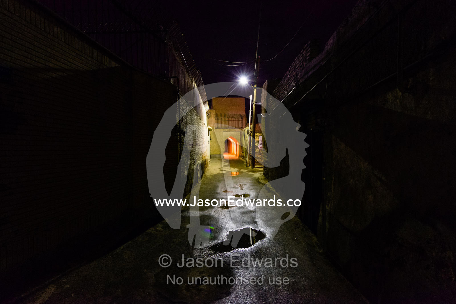 Puddles of water in a dark and narrow laneway lit by a street light. Isfahan, Isfahan Province, Islamic Republic of Iran.