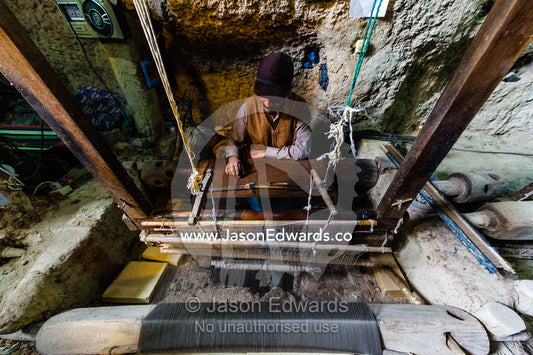 A man practicing traditional cloak weaving on an antique loom in a cave in the desert. Nain, Nain County, Isfahan Province, Iran.