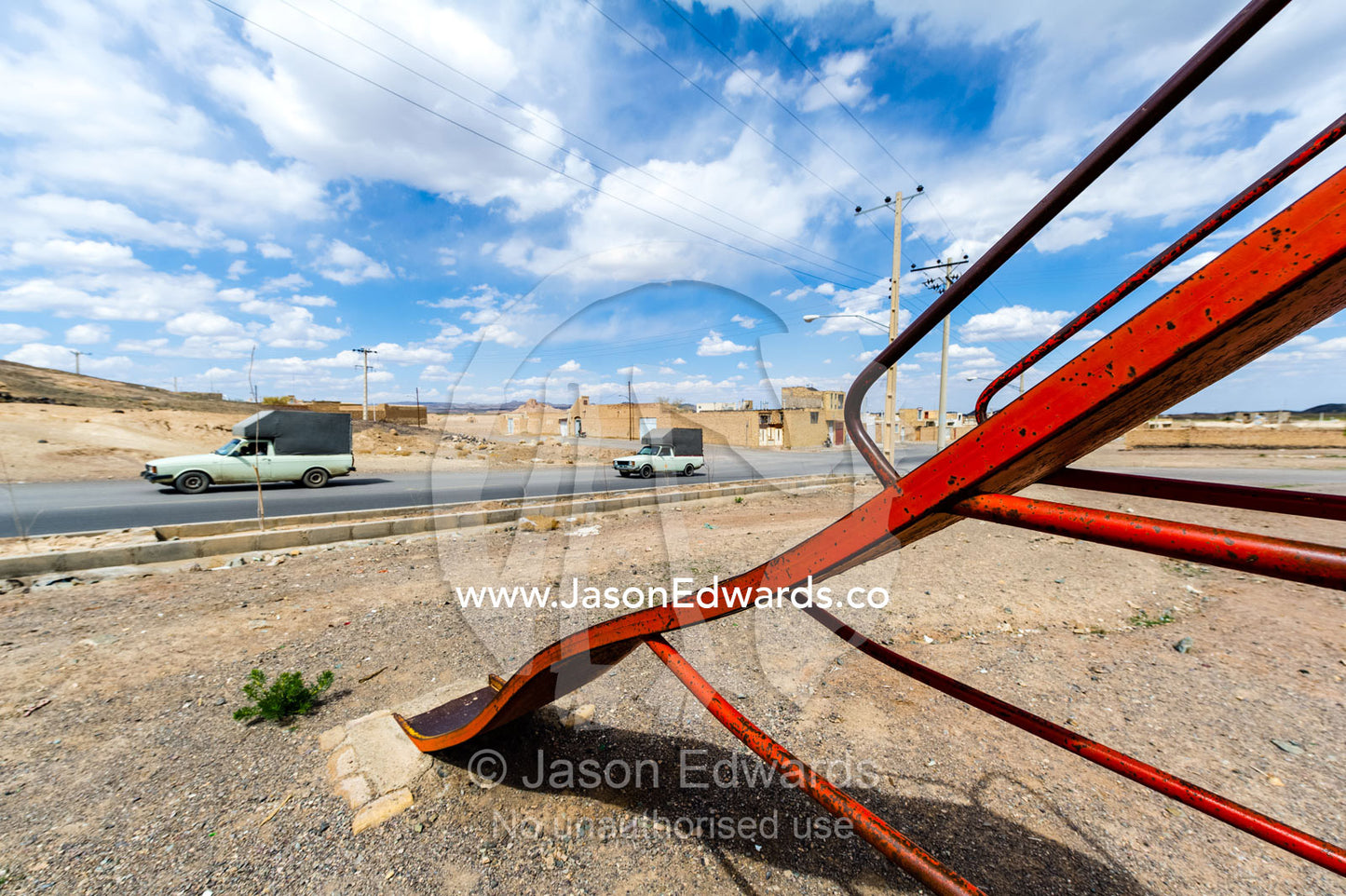 Cars transporting goods drive past a playground in a desert village. Nain, Nain County, Isfahan Province, Iran.