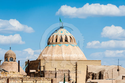 The enormous mud brick dome of a mosque beneath white fluffy clouds in Nain. Nain, Nain County, Isfahan Province, Iran.