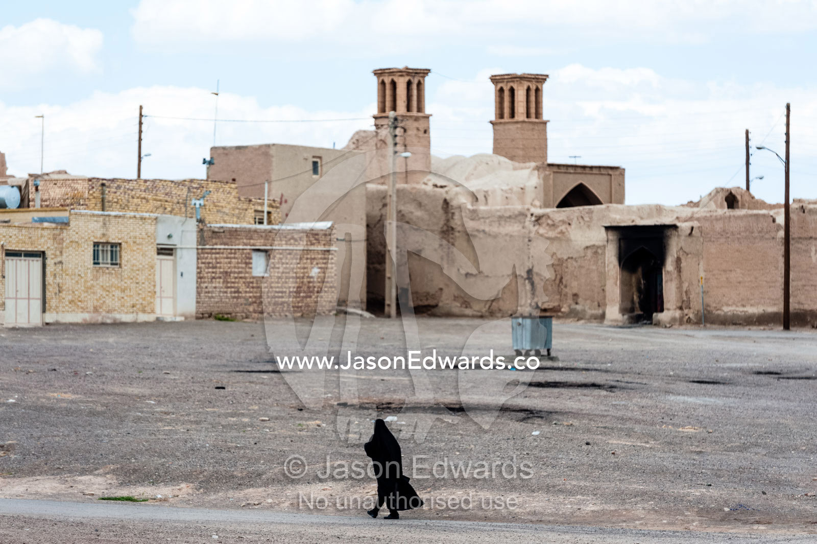 A woman in a chador moves through a deserted village beneath windcatchers. Nain, Nain County, Isfahan Province, Iran.
