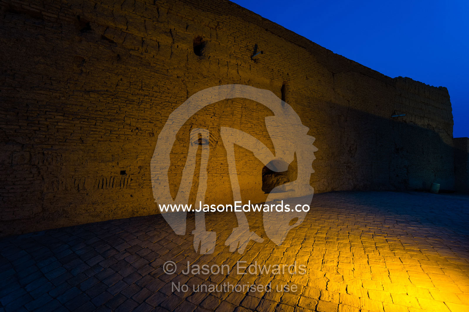 Spotlights on the imposing mud brick wall of an ancient fortress towers over the desert. Narin Castle, Meybod, Meybod County, Yazd Province, Islamic Republic of Iran.