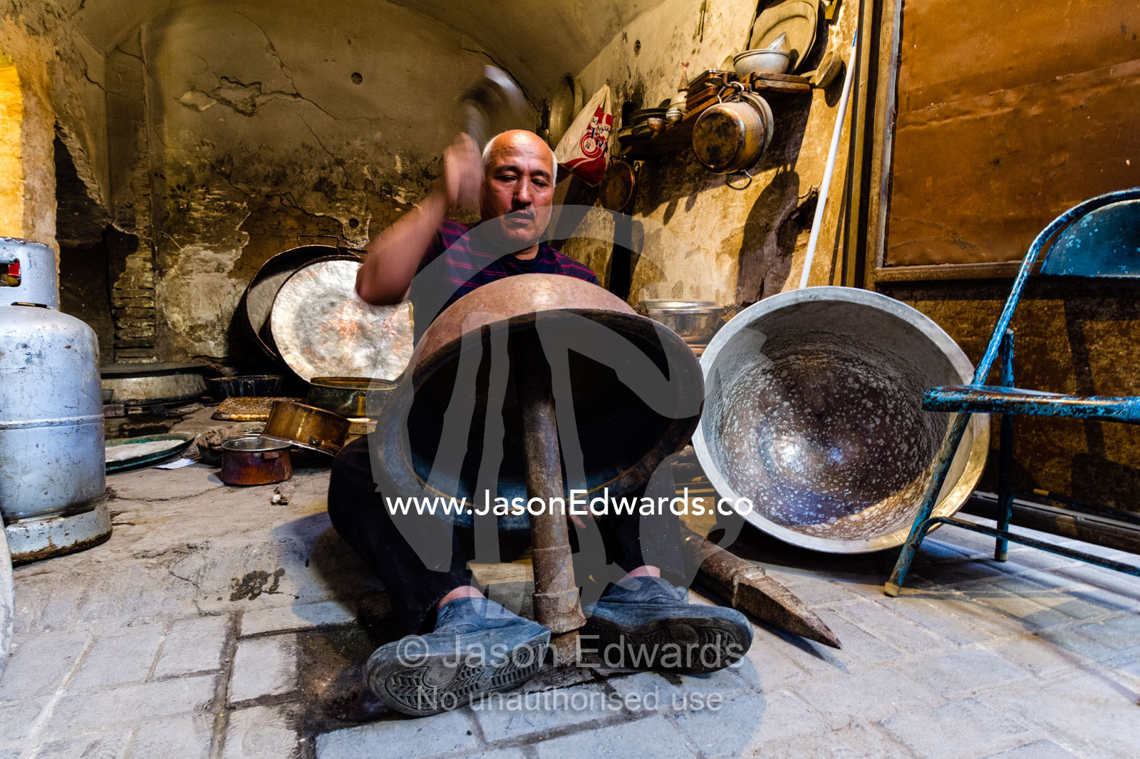 A workshop in an ancient bazaar where a potter bashes copper plate into pots. Yazd, Yazd Province, Islamic Republic of Iran.