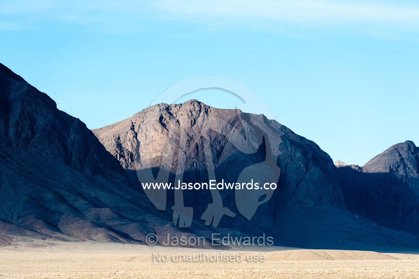 Jagged desert mountains scoured by erosion rise from a desert plain. Kharanagh, Yazd, Yazd Province, Islamic Republic of Iran.