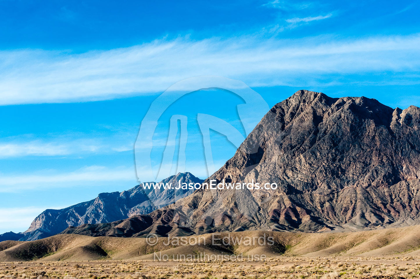 Jagged desert mountains scoured by erosion rise from a desert plain. Kharanagh, Yazd, Yazd Province, Islamic Republic of Iran.