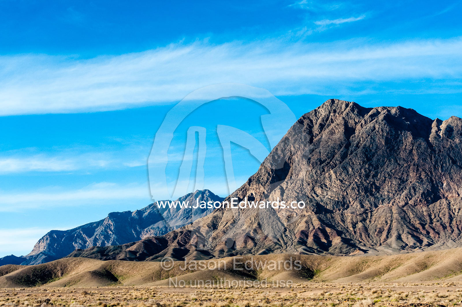 Jagged desert mountains scoured by erosion rise from a desert plain. Kharanagh, Yazd, Yazd Province, Islamic Republic of Iran.
