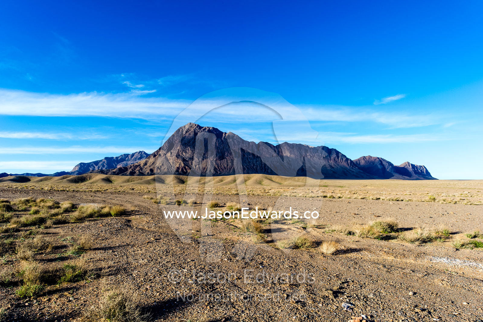 Jagged desert mountains scoured by erosion rise from a desert plain. Kharanagh, Yazd, Yazd Province, Islamic Republic of Iran.