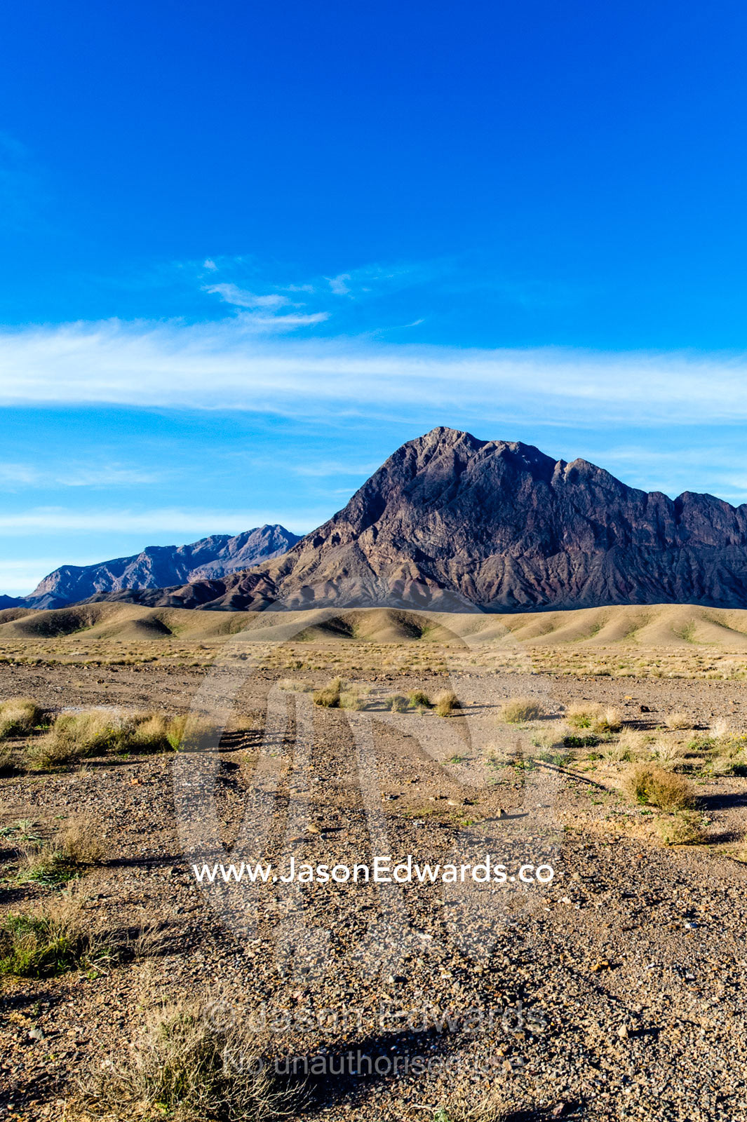 Jagged desert mountains scoured by erosion rise from a desert plain. Kharanagh, Yazd, Yazd Province, Islamic Republic of Iran.