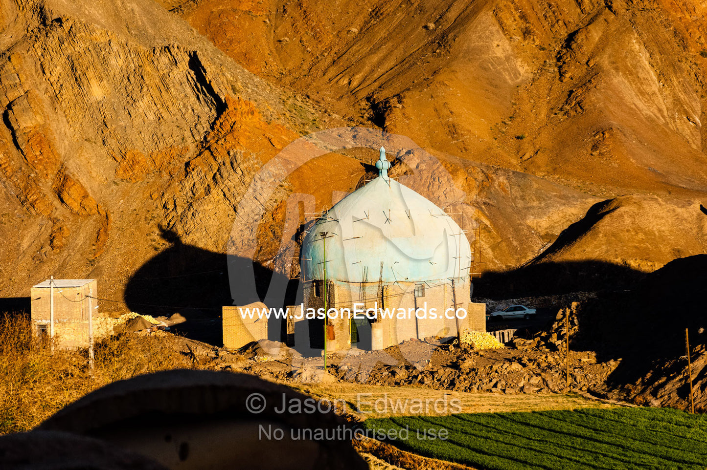 A mosque being constructed at the foot of desert mountains at sunset. Kharanagh, Yazd, Yazd Province, Islamic Republic of Iran.