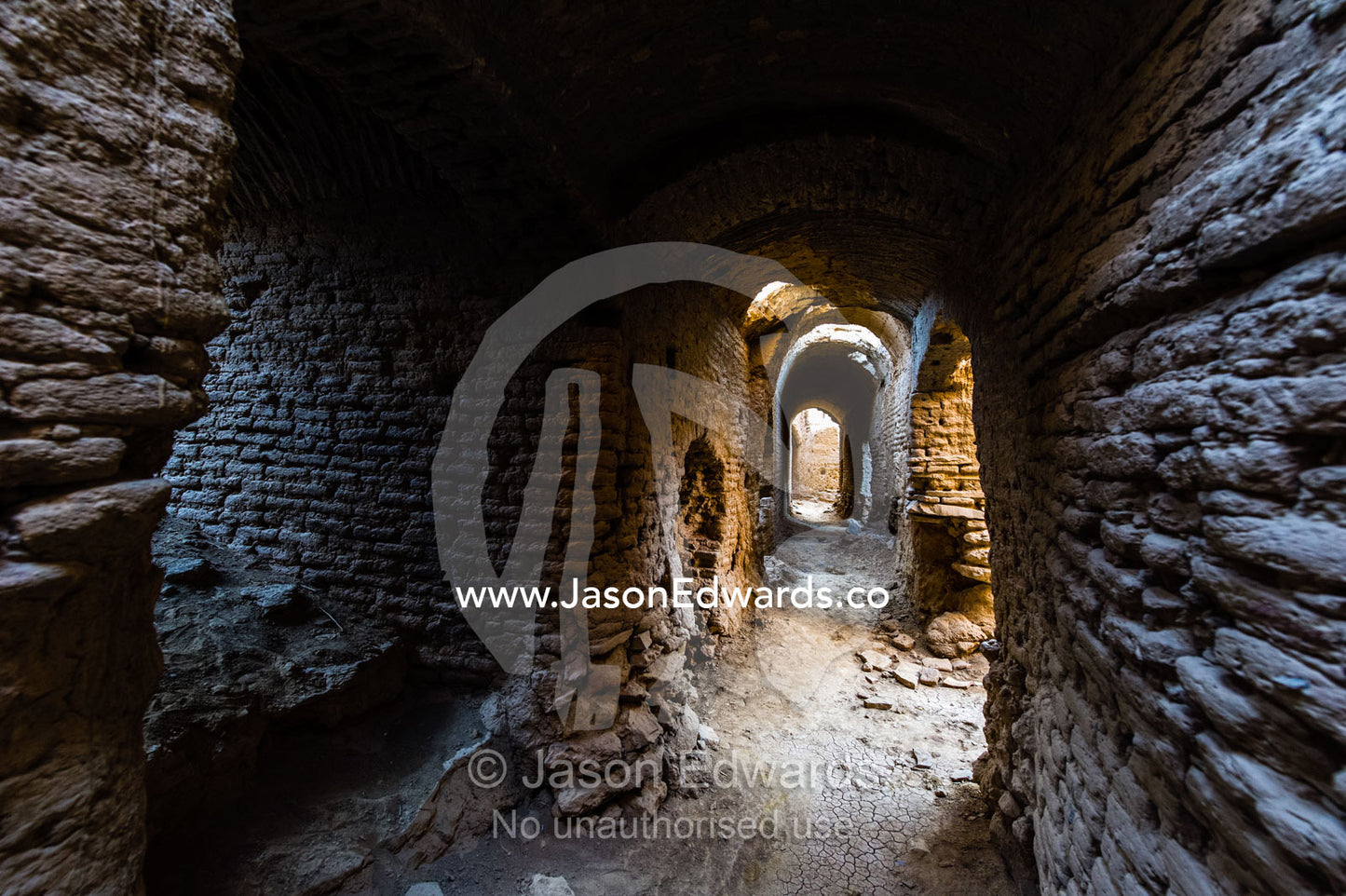 A laneway passes between buildings of crumbling handmade brick in the ruins of an ancient abandoned village in the desert. Kharanagh, Yazd, Yazd Province, Islamic Republic of Iran.