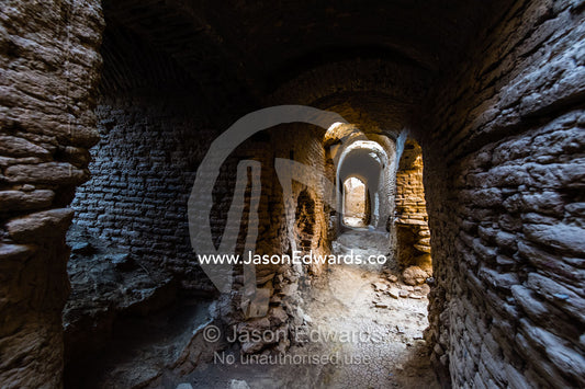 A laneway passes between buildings of crumbling handmade brick in the ruins of an ancient abandoned village in the desert. Kharanagh, Yazd, Yazd Province, Islamic Republic of Iran.