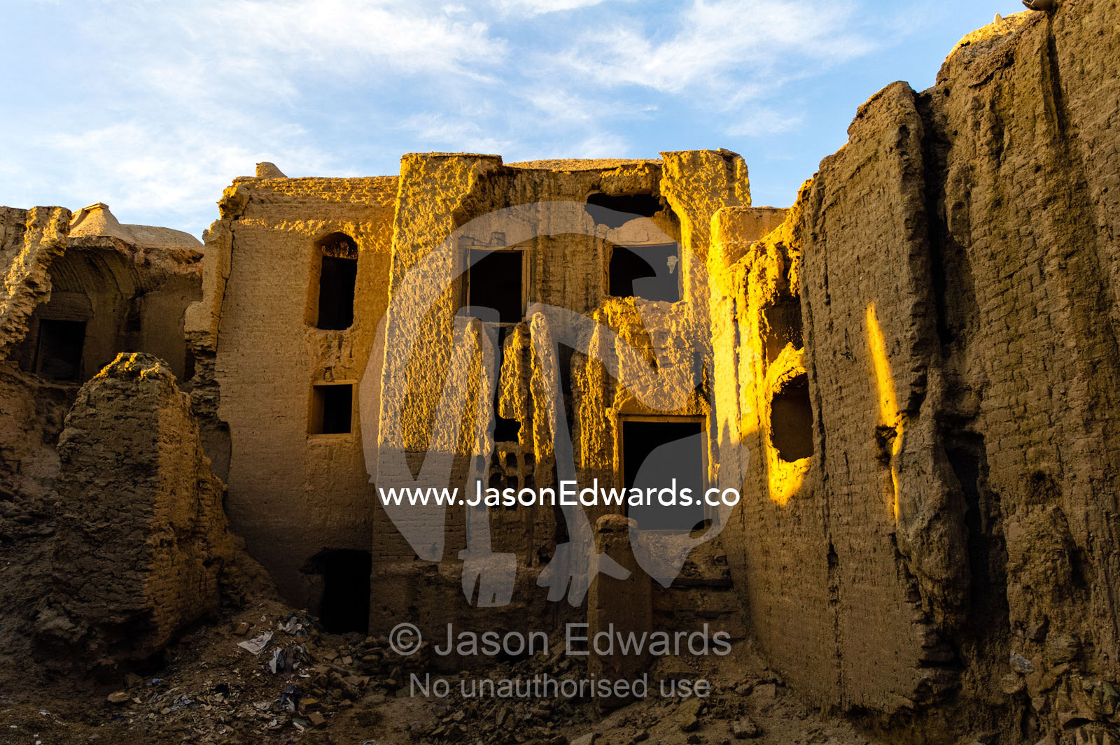 Sunset warms buildings of crumbling handmade brick ruins of an ancient abandoned village in the desert. Kharanagh, Yazd, Yazd Province, Islamic Republic of Iran.
