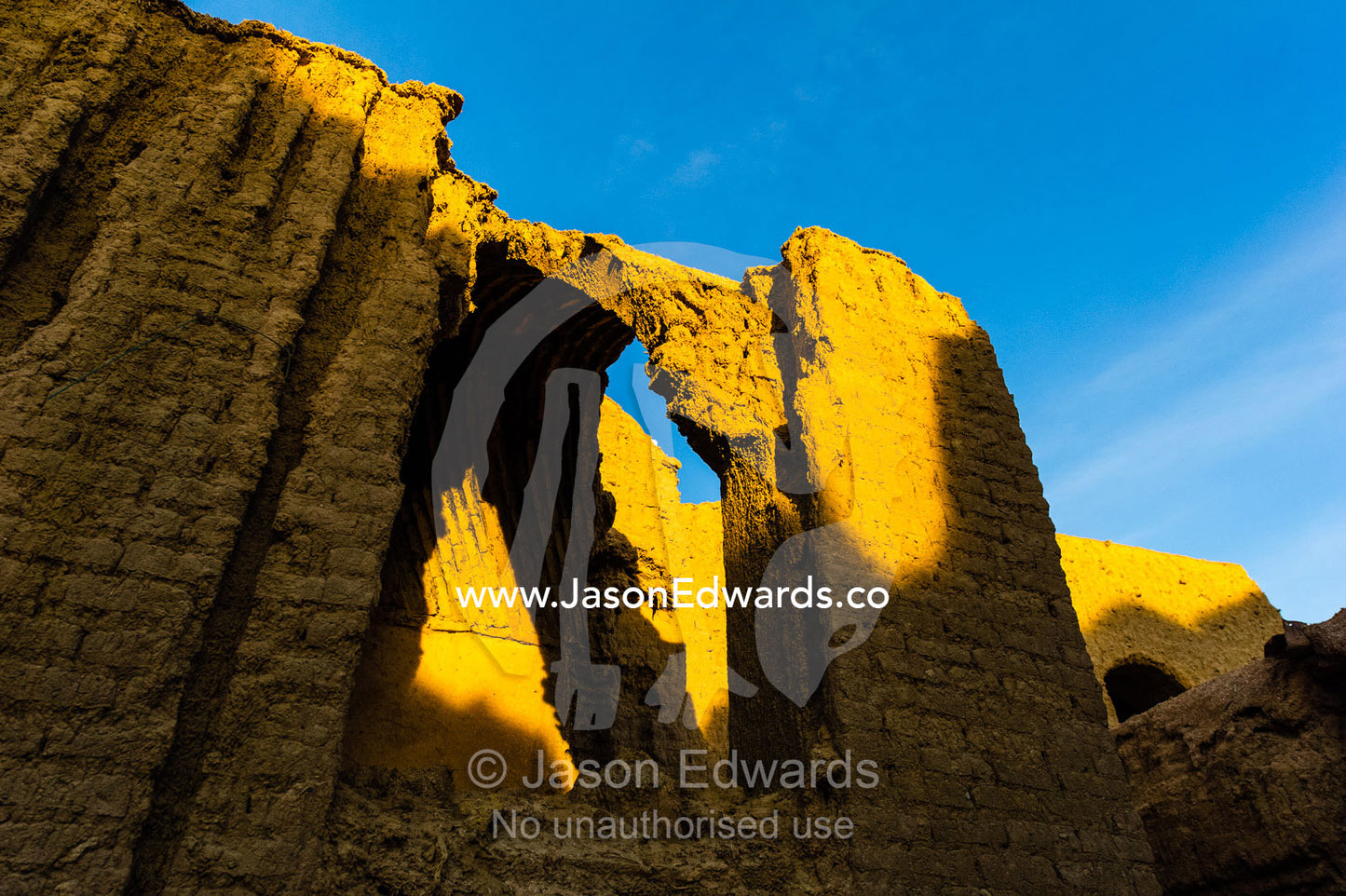 Sunset warms buildings of crumbling handmade brick ruins of an ancient abandoned village in the desert. Kharanagh, Yazd, Yazd Province, Islamic Republic of Iran.