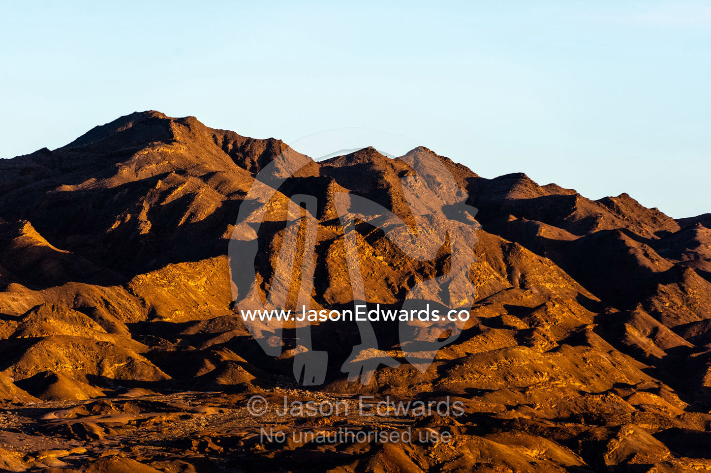 Jagged desert mountains scoured by erosion rise from a desert plain at sunset. Kharanagh, Yazd, Yazd Province, Islamic Republic of Iran.