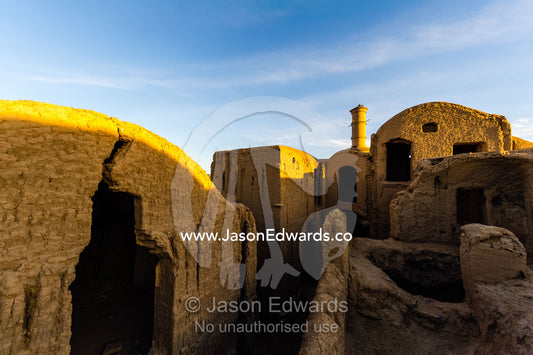 Sunset warms buildings of crumbling handmade brick ruins of an ancient abandoned village in the desert. Kharanagh, Yazd, Yazd Province, Islamic Republic of Iran.