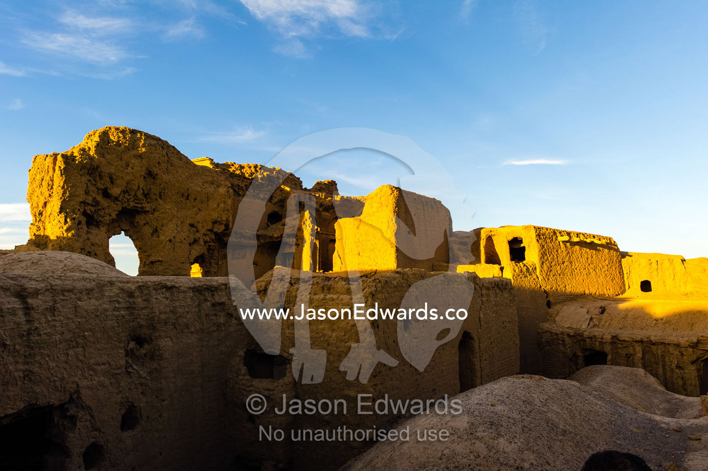 Sunset warms buildings of crumbling handmade brick ruins of an ancient abandoned village in the desert. Kharanagh, Yazd, Yazd Province, Islamic Republic of Iran.