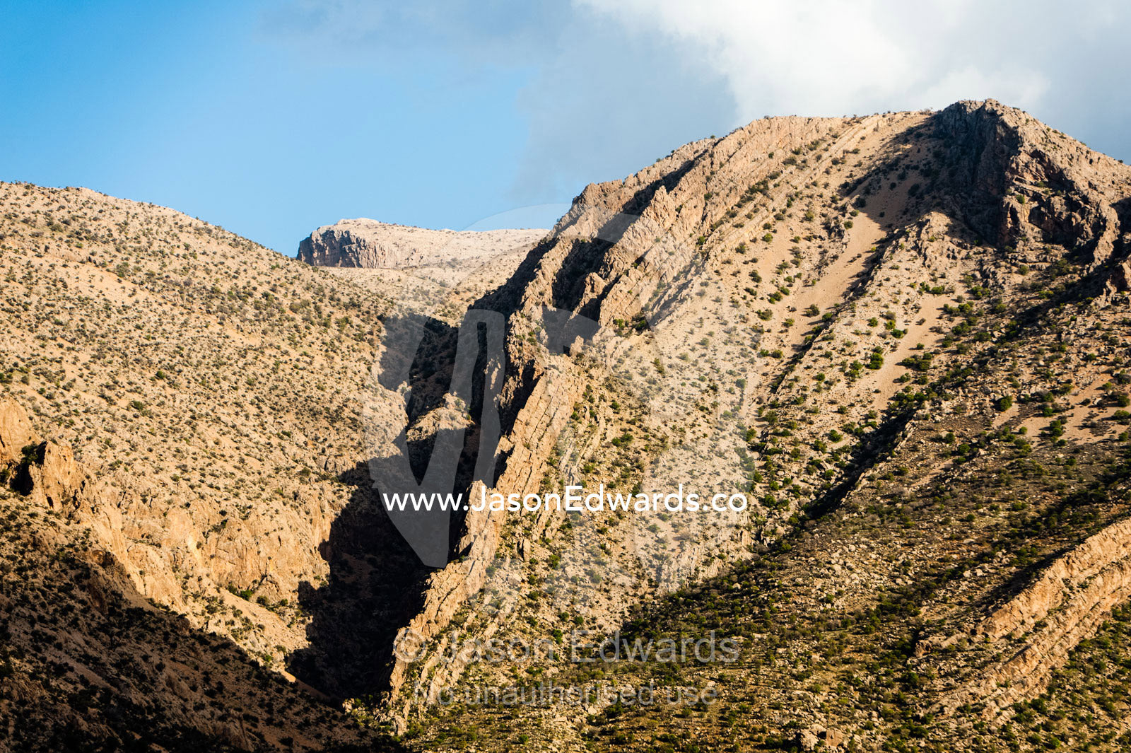 Jagged desert mountains scoured by erosion rise from a desert plain at sunset. Fars Province, Islamic Republic of Iran.