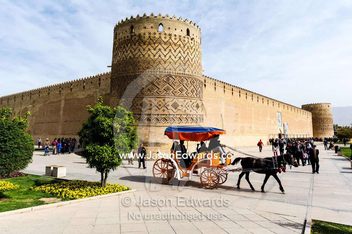 A classical colourful horse-drawn carriage passes the walls and tower of a castle. Karim Khan Castle, Shiraz, Fars Province, Islamic Republic of Iran.