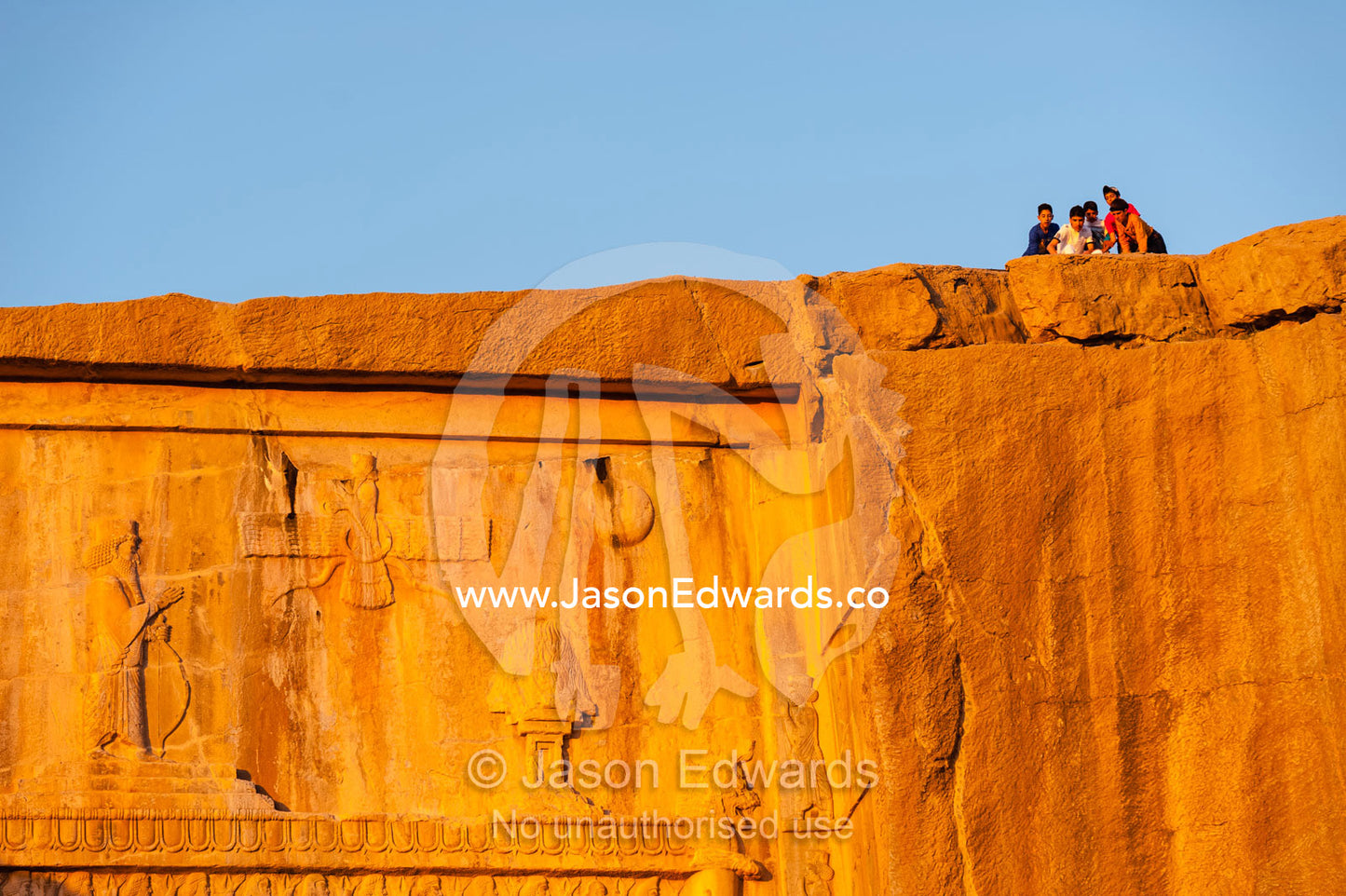 A group of teenage friends looking over the cliff above the Tomb of Artaxerxes II at sunset. Naqsh-e Rustam, Fars Province, Islamic Republic of Iran.
