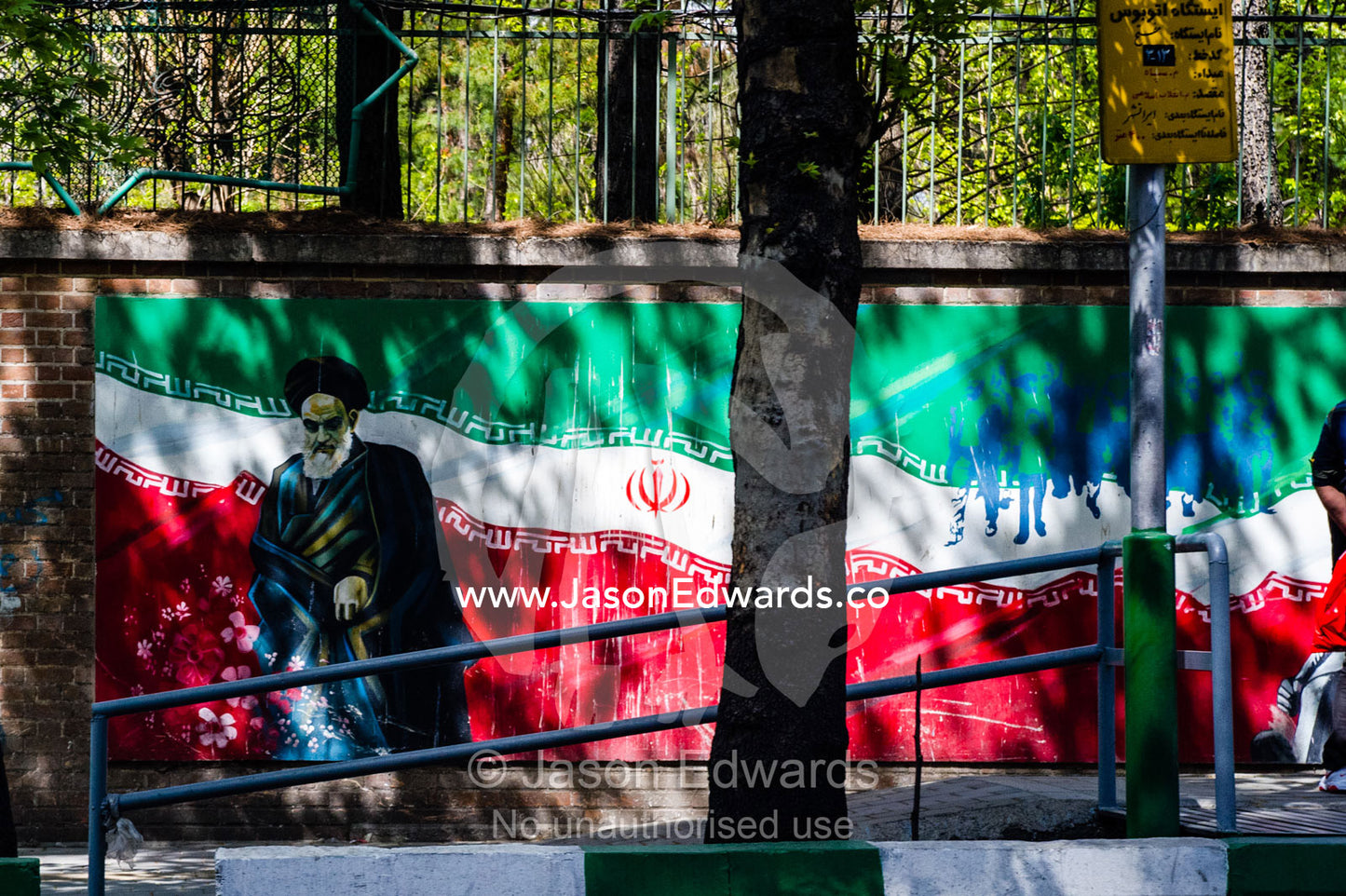 A painting of the Supreme Leader of Iran Ayatollah Khomeini, flowers and the Iranian flag on the wall of the ex-US Embassy in Tehran. Tehran, Tehran Province, Islamic Republic of Iran.
