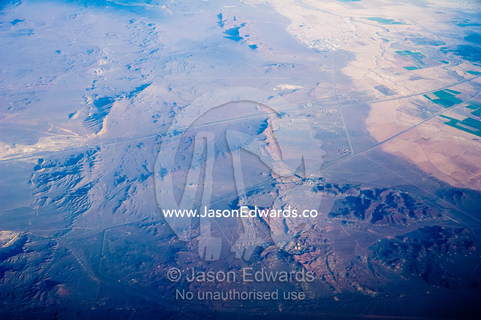 A high altitude view of sunrays lighting jagged mountain peaks and a village in the desert. Islamic Republic of Iran.