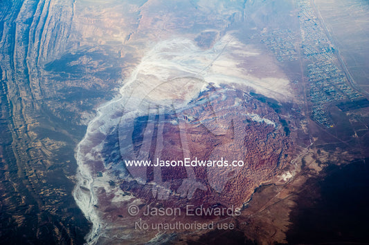 A high altitude view of sunrays lighting jagged mountain peaks and a salt lake near a village in the desert. Islamic Republic of Iran.