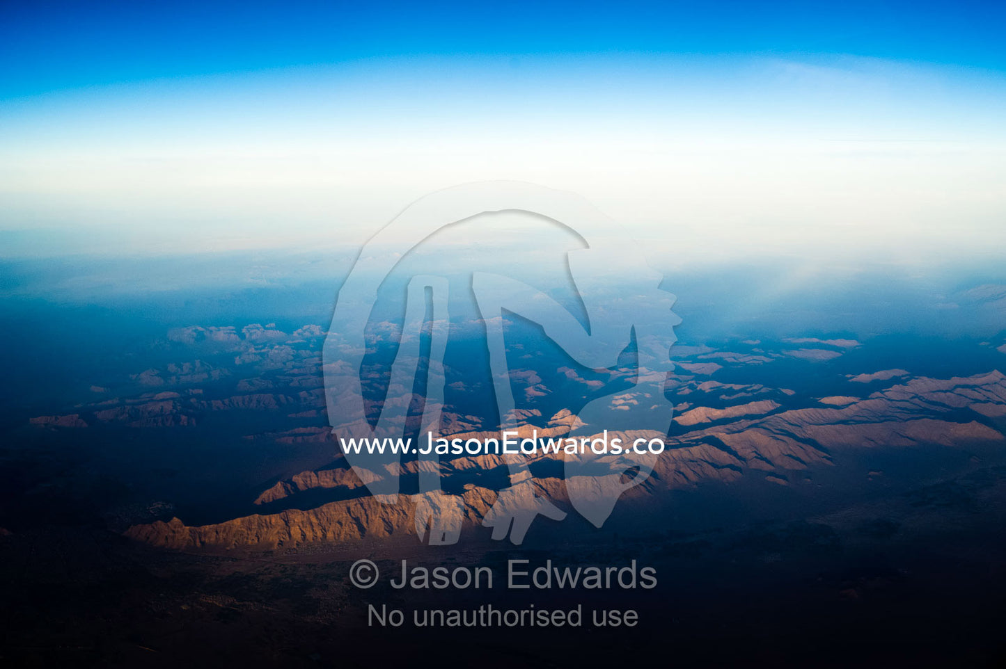 A high altitude view of sunrays lighting jagged mountain peaks in the desert. Islamic Republic of Iran.