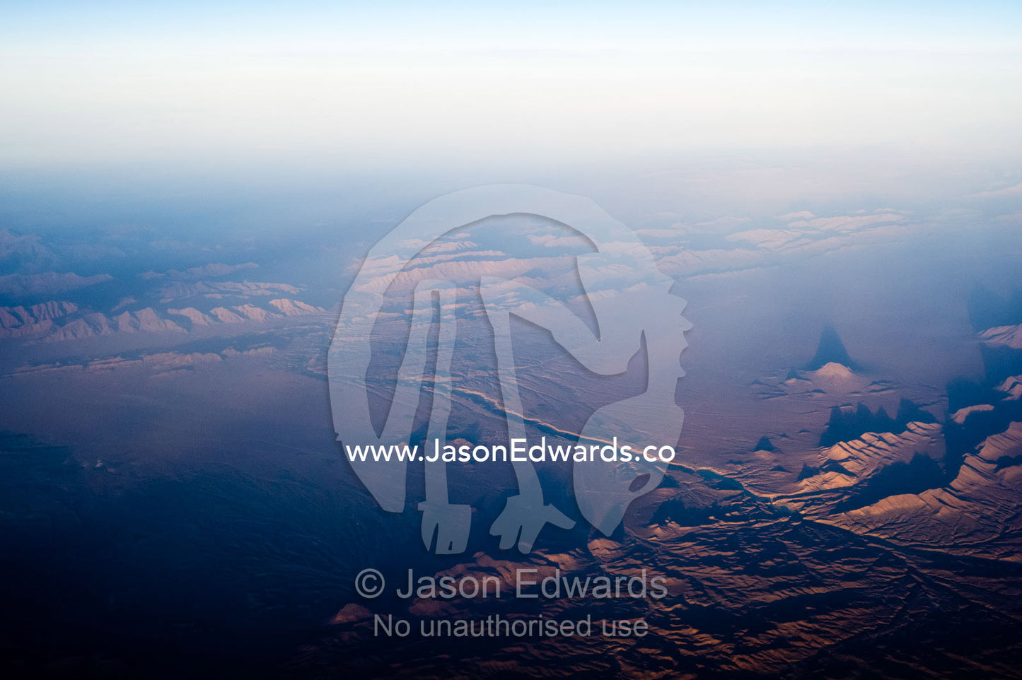 A high altitude view of sunrays lighting jagged mountain peaks in the desert. Islamic Republic of Iran.