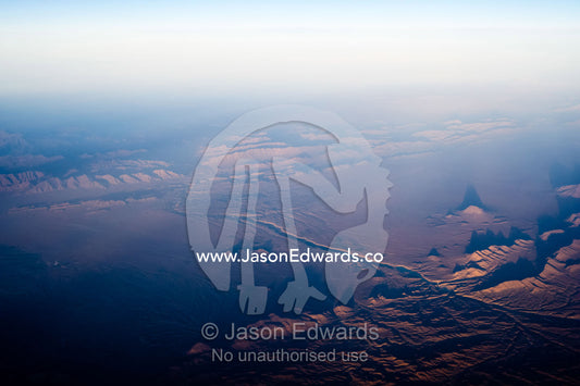 A high altitude view of sunrays lighting jagged mountain peaks in the desert. Islamic Republic of Iran.