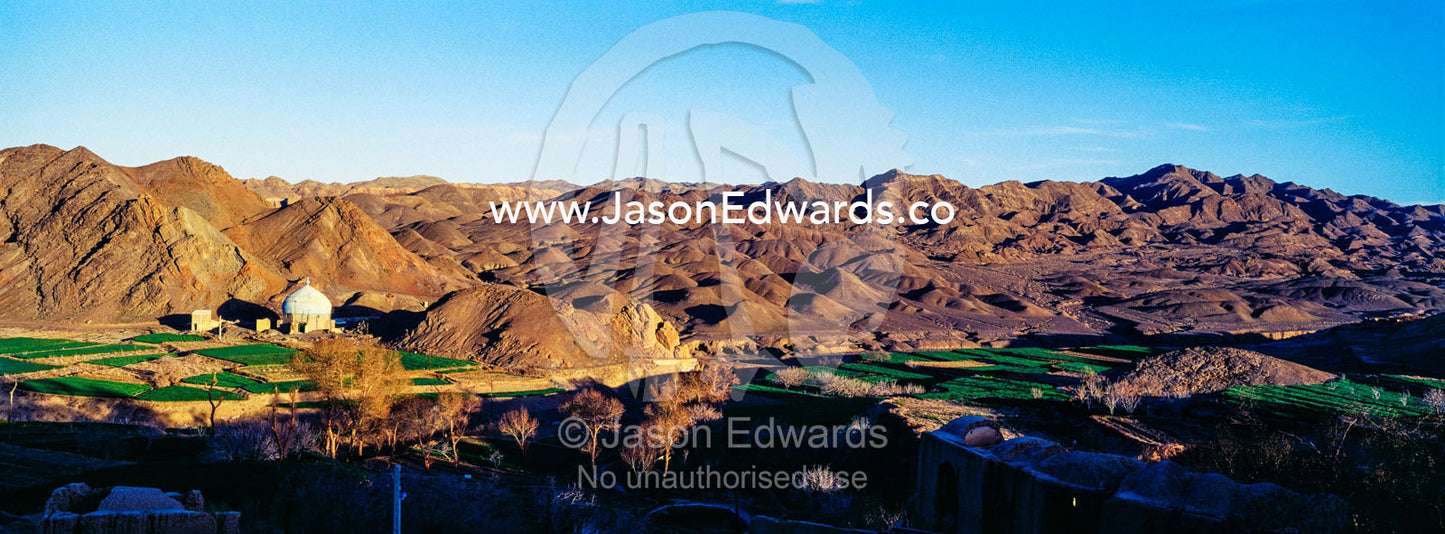 A mosque being constructed at the foot of desert mountains at sunset. Kharanagh, Yazd, Yazd Province, Islamic Republic of Iran.