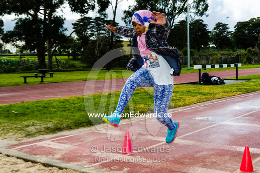 A girl wearing a hijab leaps through the air doing a long jump at an elementary school athletics competition. Collingwood, Melbourne, Victoria, Australia.