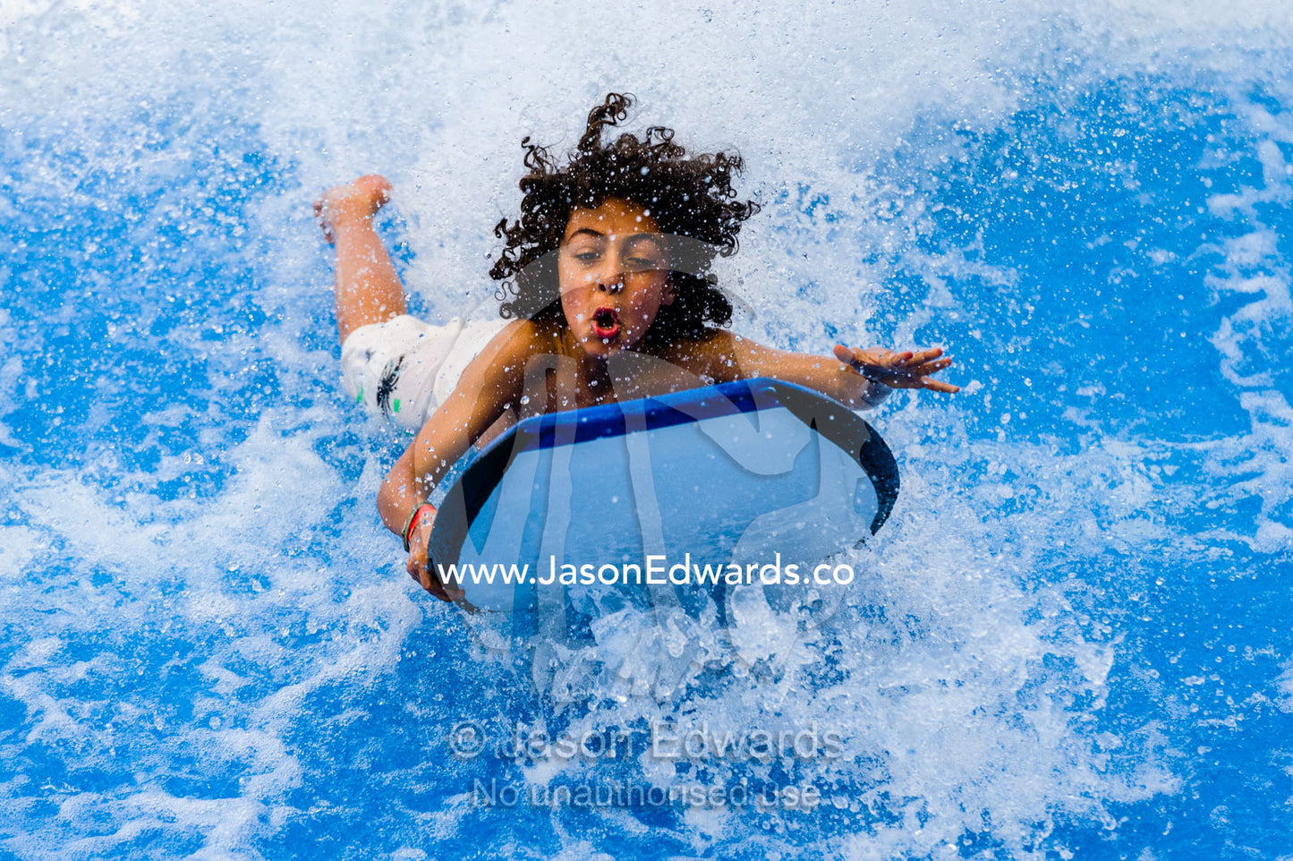 A boy rides a bodyboard on a artificial wave machine at a swimming pool. Melbourne Sports and Aquatic Centre, Melbourne, Victoria, Australia.