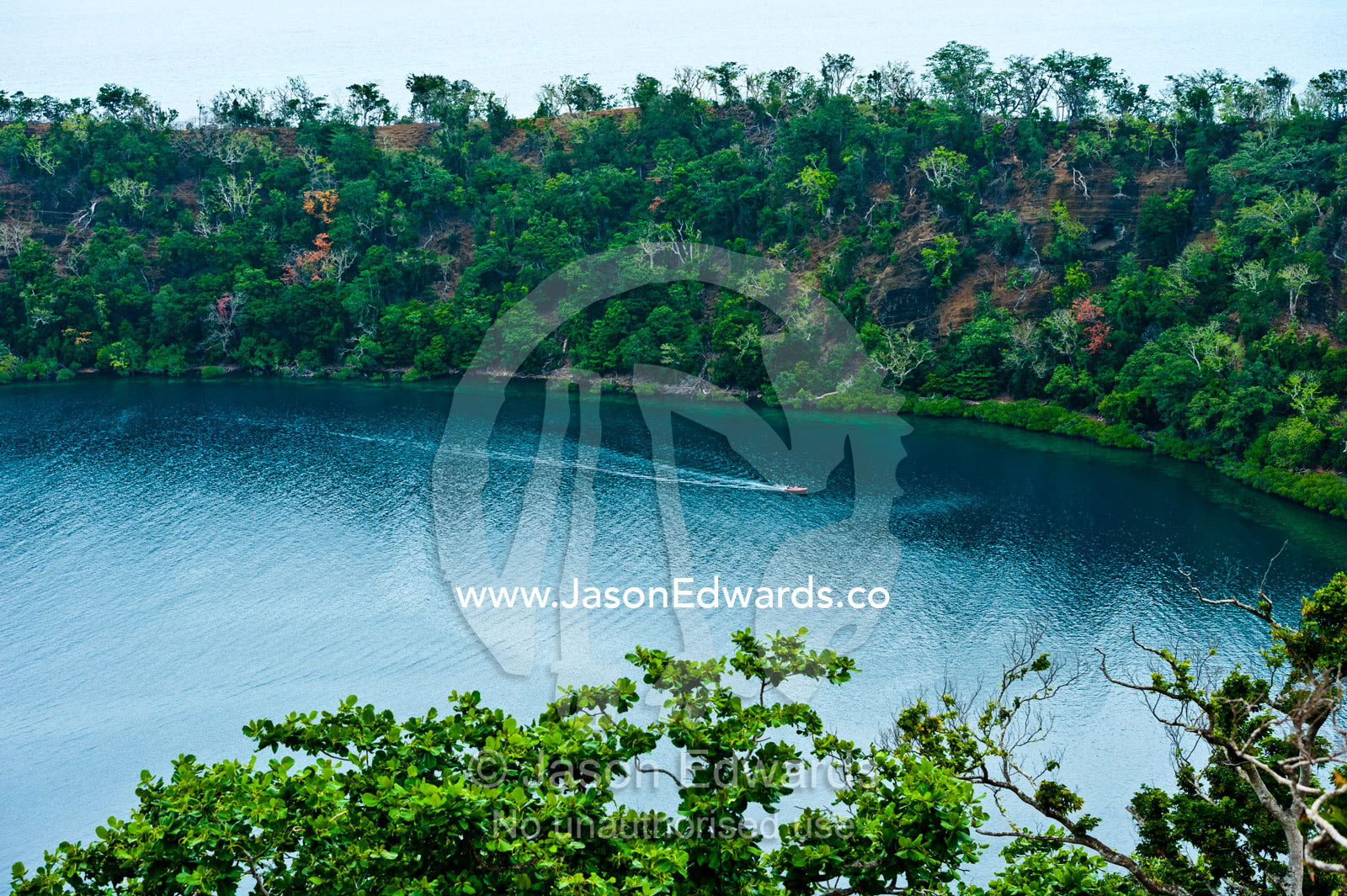 A tiny boat explores an extinct volcano caldera covered in forest. Cobia Crater, Cobia Island, Ringgold Atolls, Pacific Ocean, Fiji Islands.