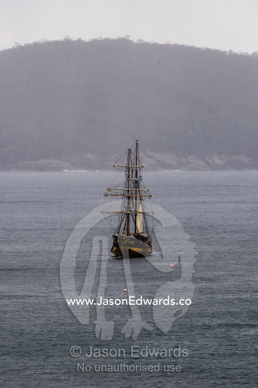 An antique sailing ship the Lady Nelson mooring in a bay on a rainy day. Mason Cove, Port Arthur Historic Site, Port Arthur, Tasmania,
Australia.