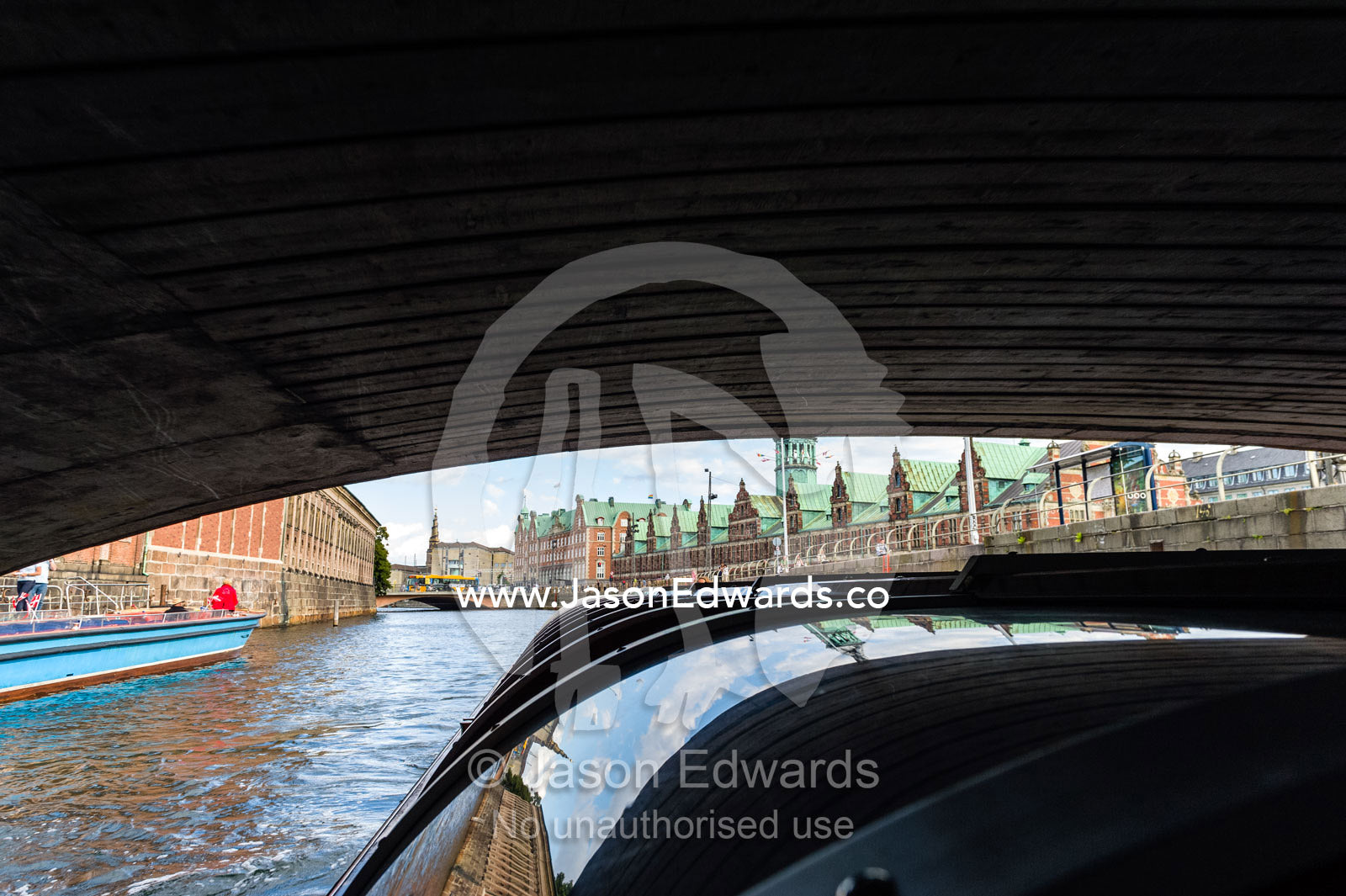 A canal boat passes beneath a low bridge exploring Copenhagen on a cruise. Copenhagen, Denmark.