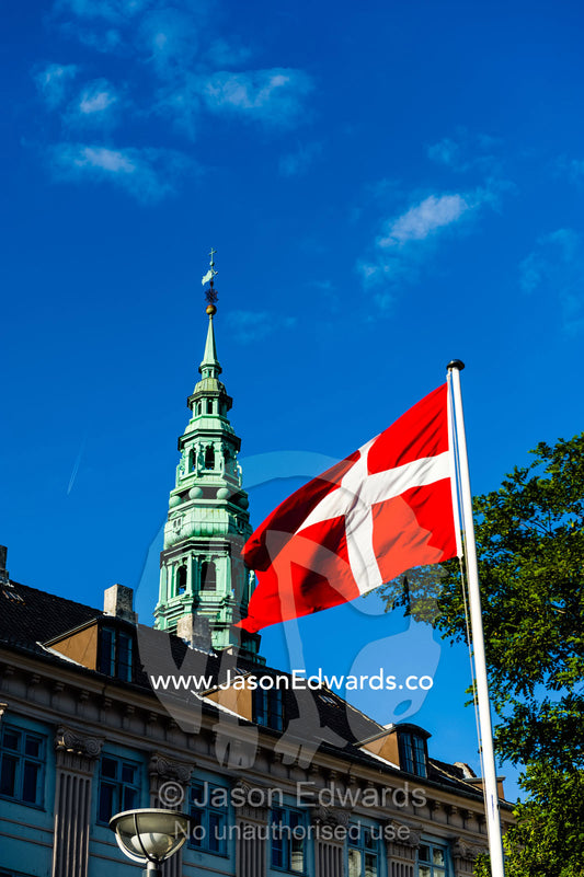 A Danish flag flutters in the breeze beneath a church spire. Nikolaj Church, Copenhagen, Denmark.