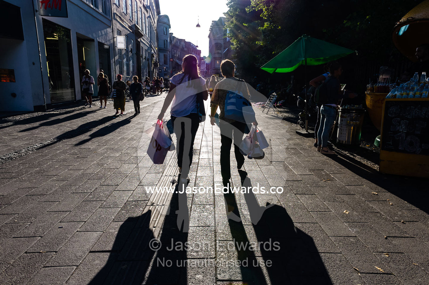 Long shadows cast by pedestrians carrying bags in a shopping district. Copenhagen, Denmark.