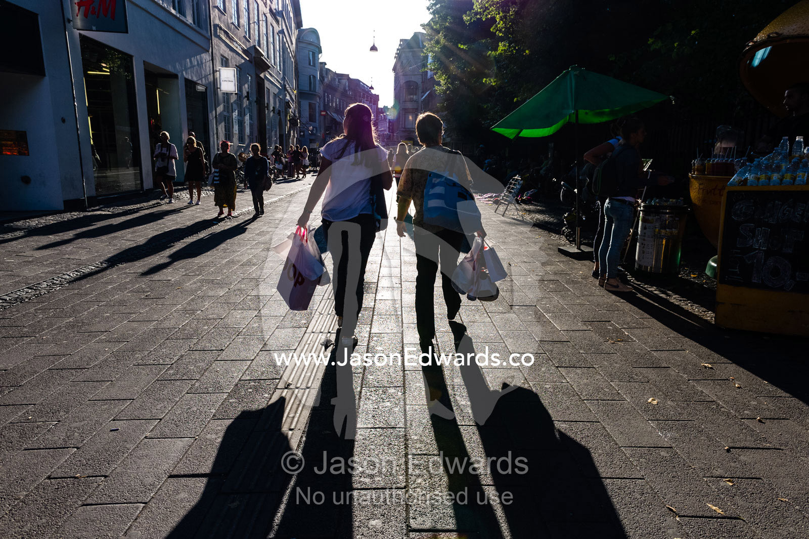 Long shadows cast by pedestrians carrying bags in a shopping district. Copenhagen, Denmark.