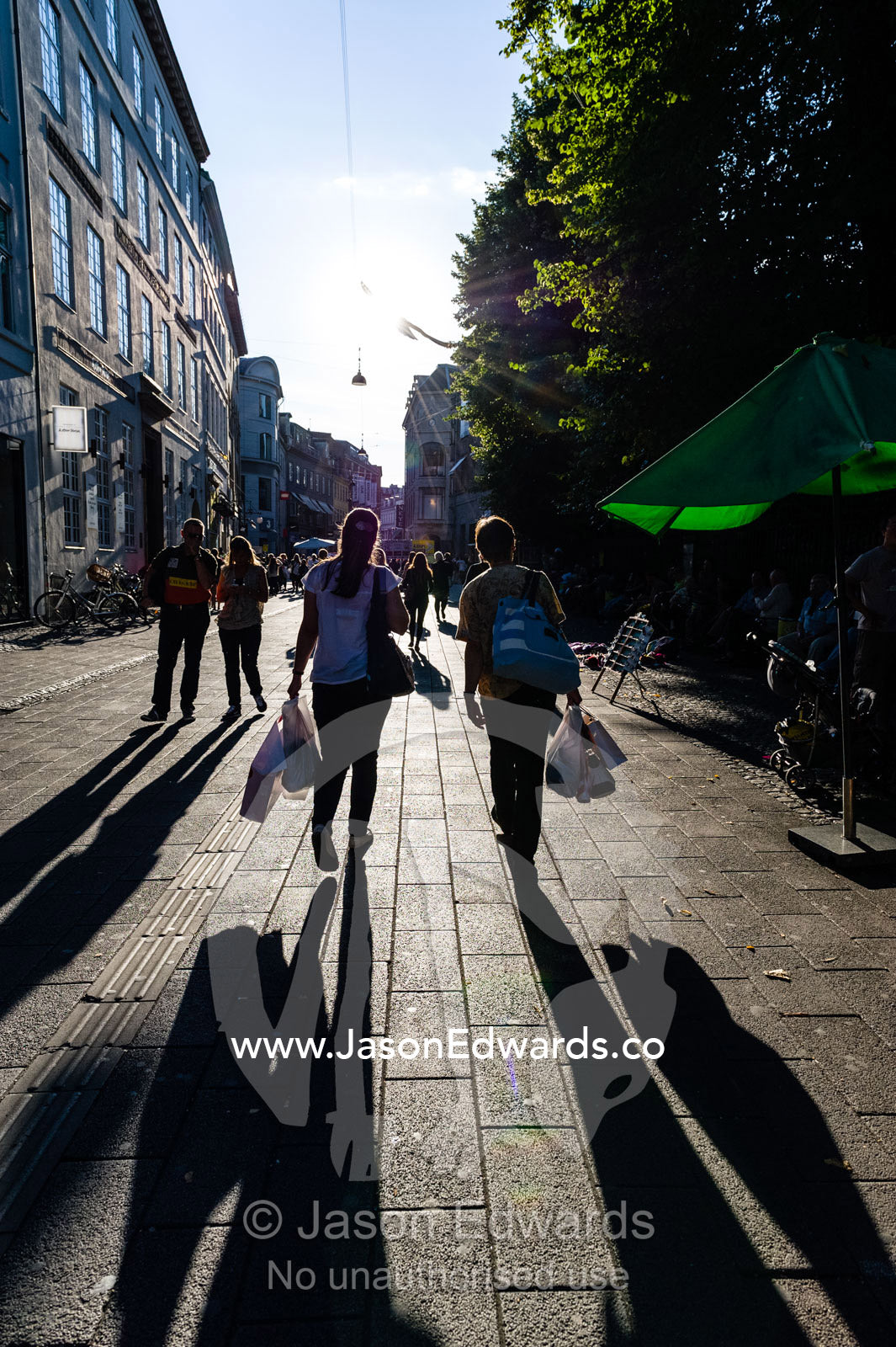 Long shadows cast by pedestrians carrying bags in a shopping district. Copenhagen, Denmark.